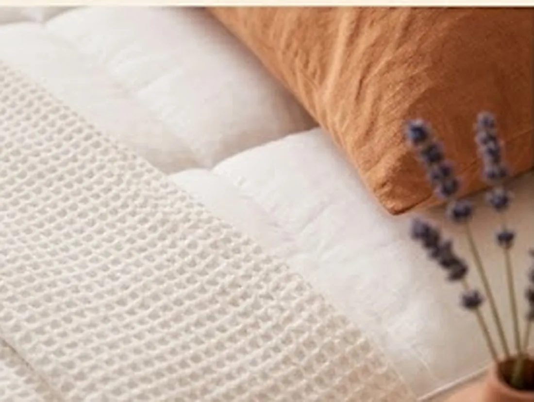 Détail de matières : surmatelas matelassé, plaid gaufré et coussin terracotta